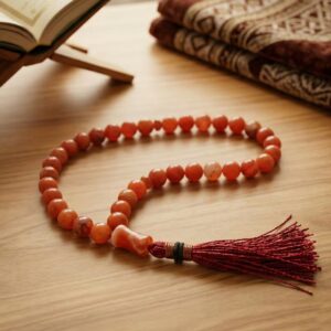 Red Aqeeq tasbeeh placed on prayer mat Islamic setting